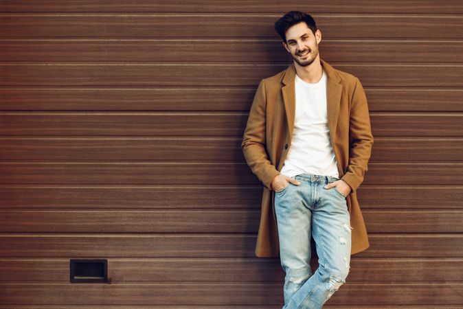 Smiling male with beard in smart winter jacket in front of brown wall