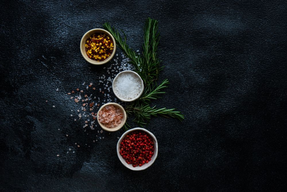 Top view of salt and seasoning bowls and rosemary on kitchen counter with copy space