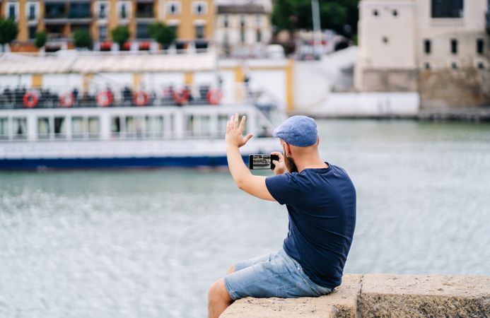 Guy on vacation in casual clothing making photo of bay on smartphone at quay