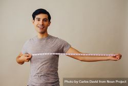 Smiling Hispanic male holding out measuring tape out to his side in beige studio shoot 41gvl0
