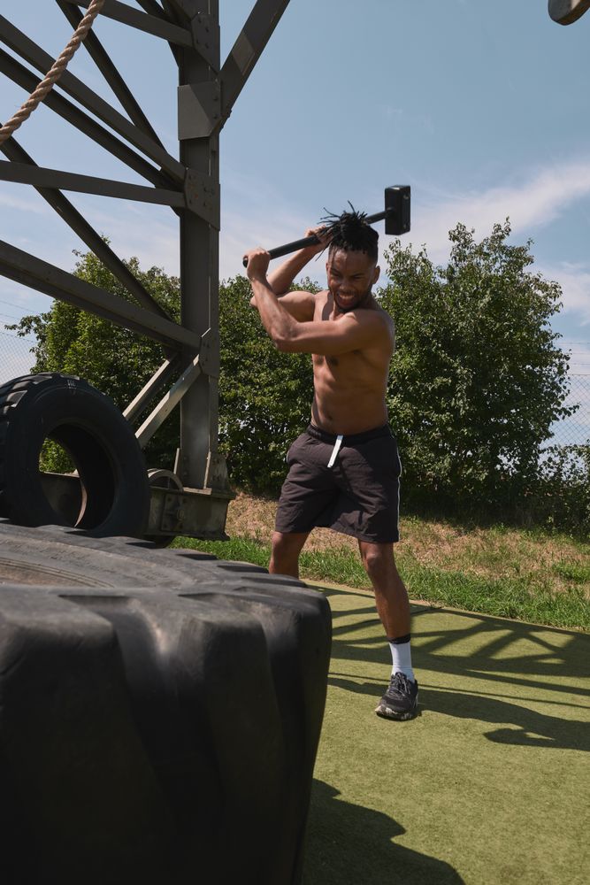 Muscular Black guy hammering tire in outdoor gym