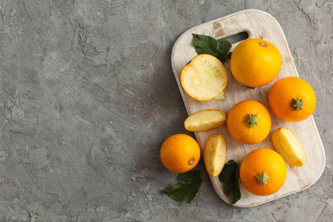 Board with round zucchini and leaves on gray background