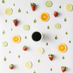 Colorful pattern made of citrus fruits, leaves and strawberries with cup of coffee