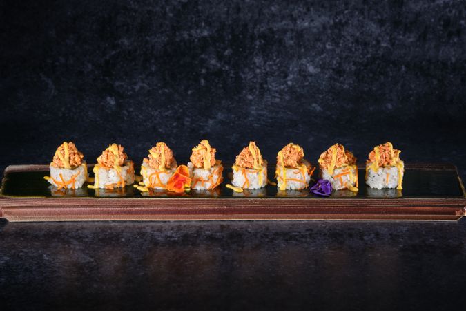 Appetizing sushi topped with salmon and fresh sauce served on wooden tray placed on table