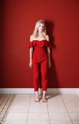 Beautiful young adult woman wearing red jumpsuit standing in red studio