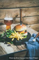 Classic hamburger skewered with knife with fries and beer at wooden restaurant table 4Bj1X4