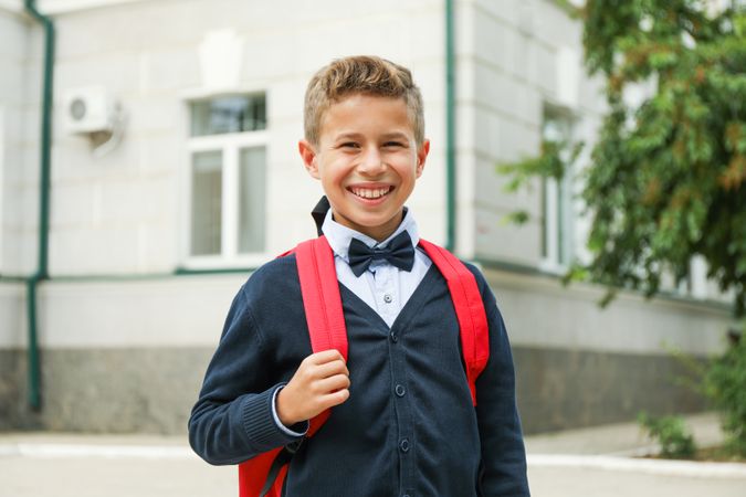 Boy with backpack against school building, space for text