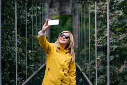 Happy female traveler taking selfie on suspension bridge in summer