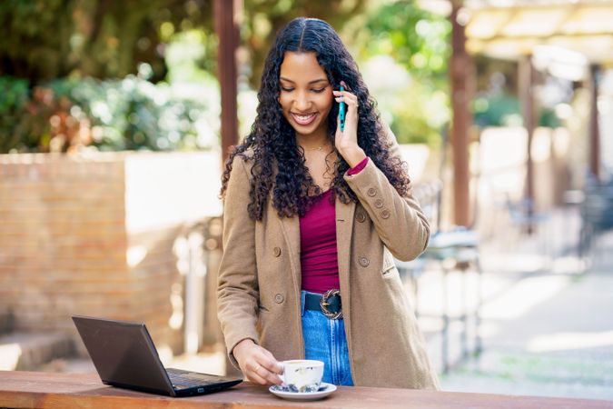 A Young Woman is Actively Working Outdoors While Enjoying a Laptop and a Warm Cup of Coffee
