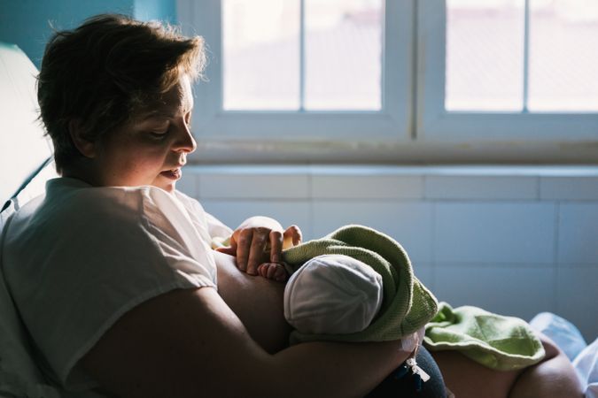Woman breastfeeding baby sitting on bed in the hospital room.