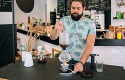 Barista skillfully stirring with spoon a specialty coffee into siphon of Japanese coffee maker