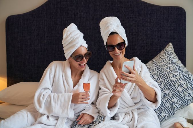 Happy women in bathrobe sitting on bed and taking selfie