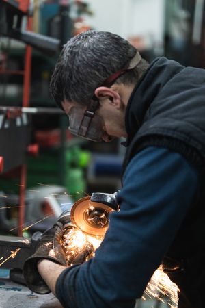 Attentive repairman cutting metal with electric grinder in workshop