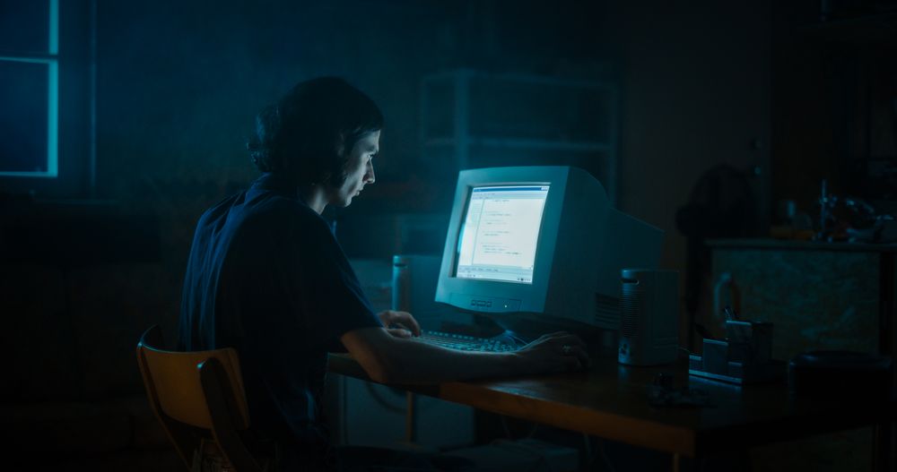 Male Web Designer Using Old Desktop Computer In Retro Garage Late At Night.