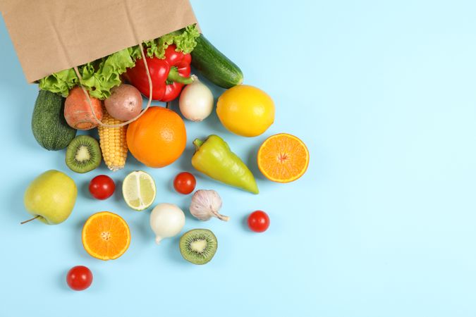 Paper bag, vegetables and fruits on blue background, space for text