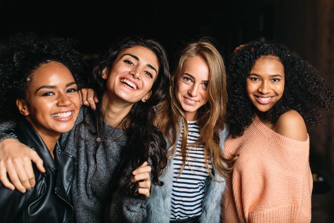 Multi-ethnic group of smiling women embracing outside at night