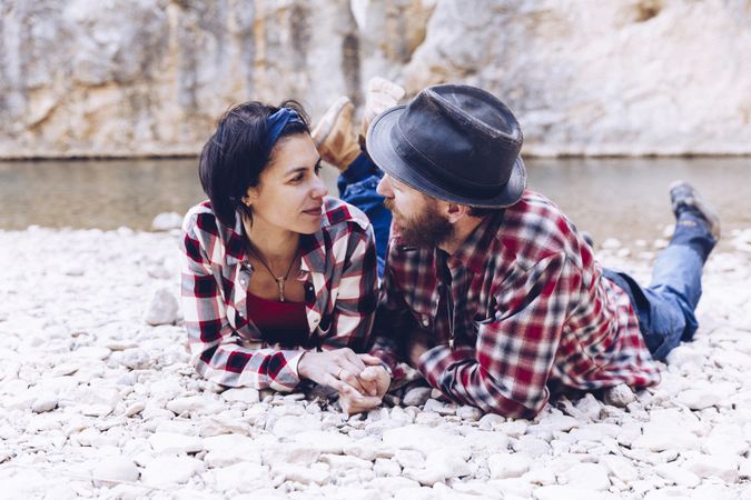 Positive woman and man resting on stone shore near river