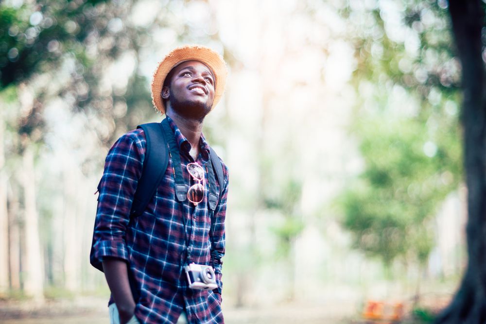 Smiling young man with camera standing beside trees