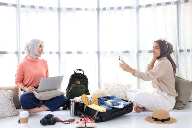 Two Young Asian Women Prepare for Summer Trip, Book Tickets Using Laptop and Take Selfies for Today's Outfits