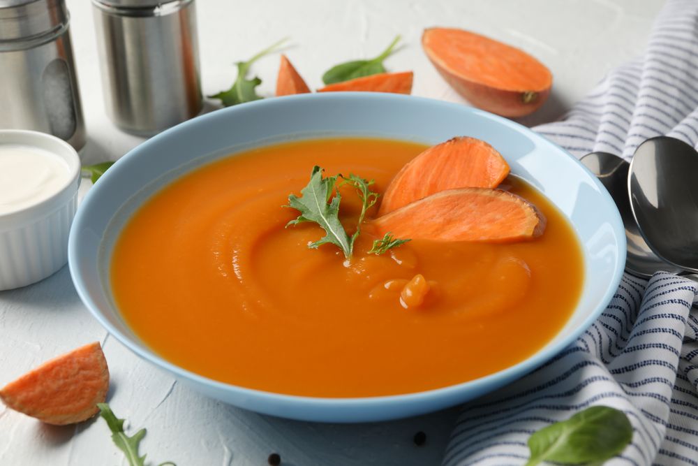 Bowl of sweet potato soup on table with salt pepper and spoons