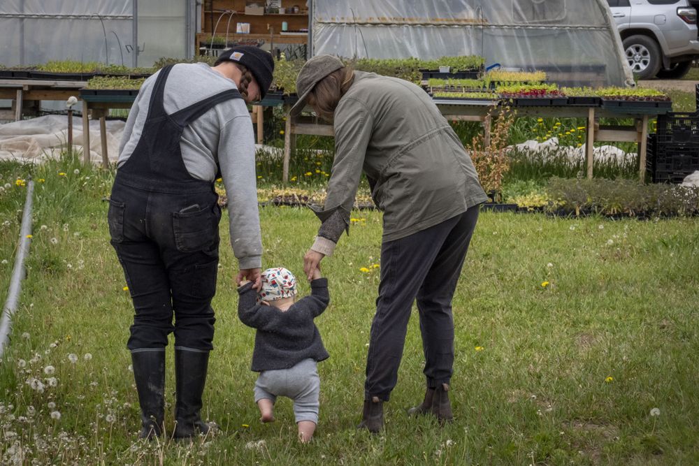 Back of two woman with a baby walking in the grass with green house