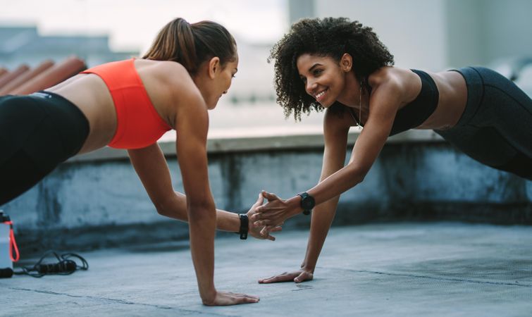 Smiling fitness women doing push ups on rooftop facing each other