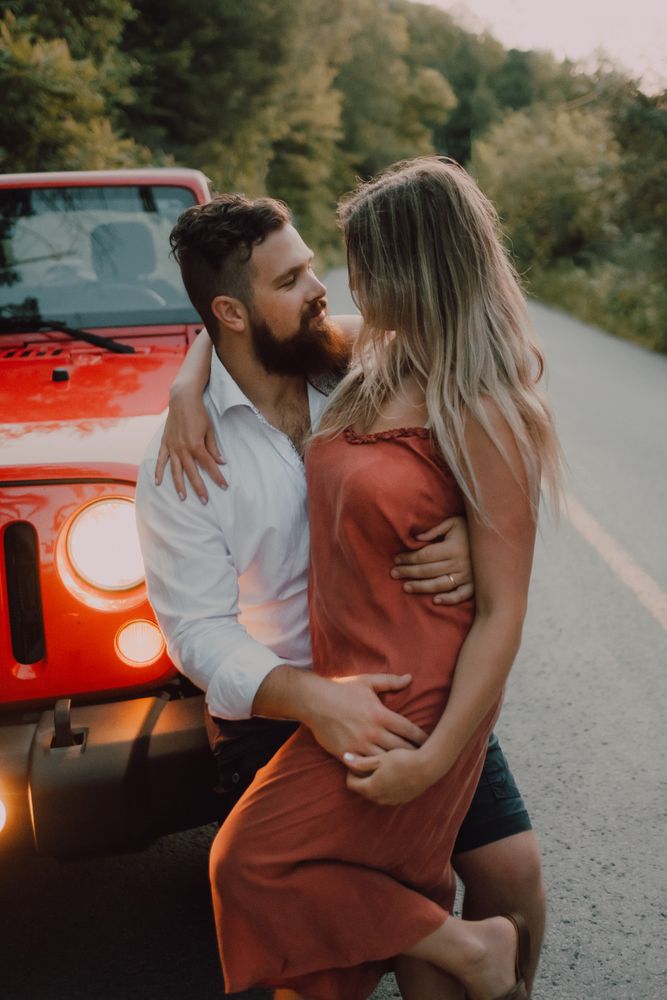 Loving couple sitting on car on road near forest