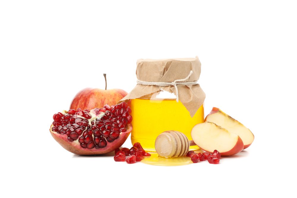 Side view of honey pot with dipper with pomegranate, and an apple quarters