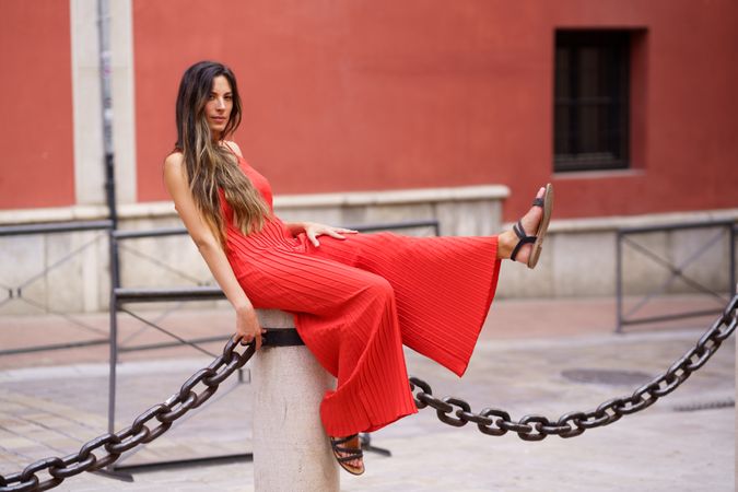 A Stylish Woman Dressed in a Beautiful Red Dress Posing Elegantly on a Chain Structure