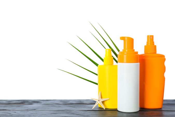 Sunscreen sprays with starfish and palm leaf on wooden table isolated on studio background. Safe tan accessories