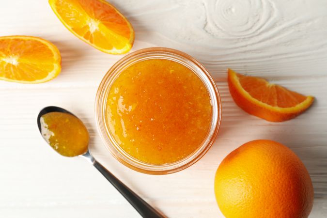 Oranges, spoon and glass jar with jam on wooden background