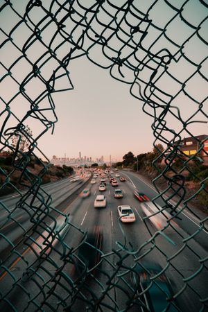 Long shot of cars on road through net fence during golden hours