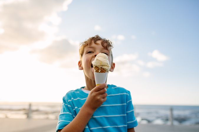 Boy eating an ice cream standing near seafront