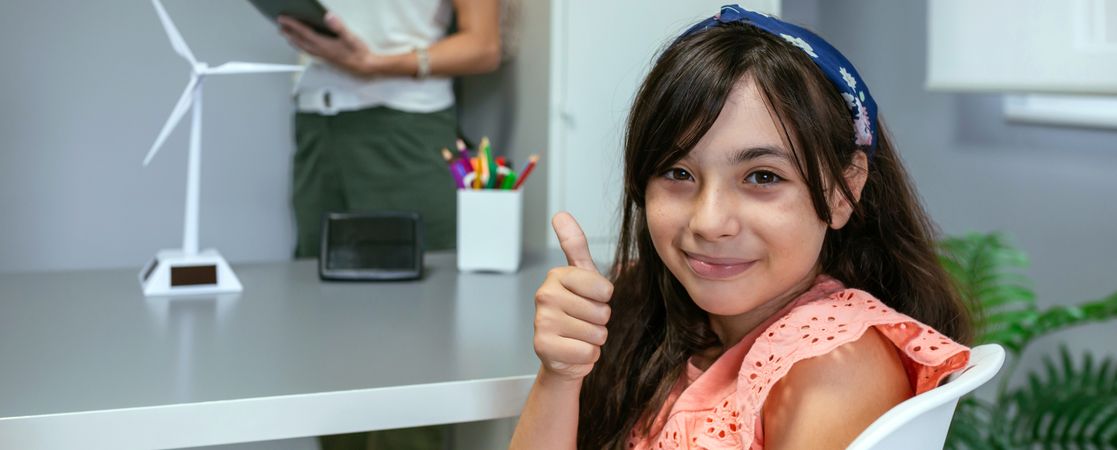 Portrait of schoolgirl in ecology classroom and teacher explaining lesson on background
