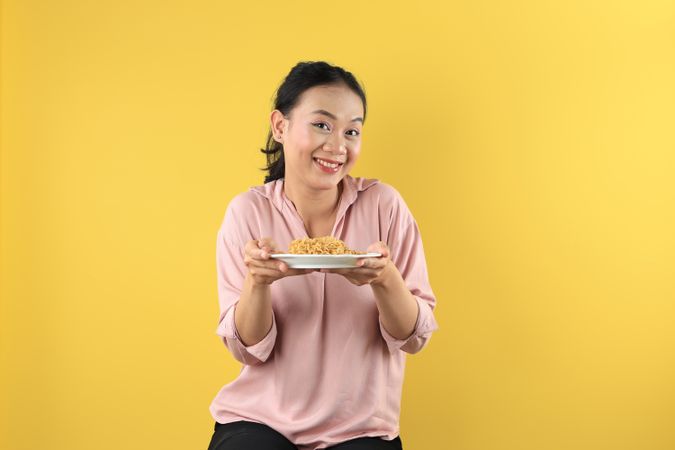 Asian Young Woman in Peach Shirt Holds a Plate of Mie Goreng Noodles with Happy Face.