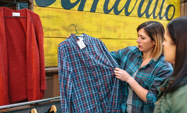 Blonde woman employee showing plaid shirt to customer in vintage store