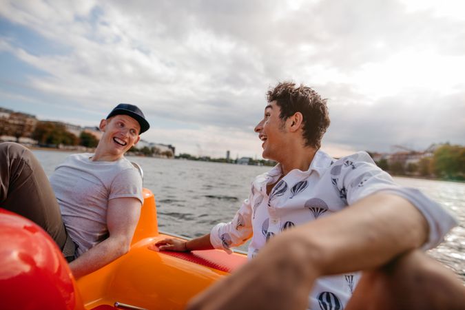 Two young men sitting in pedal boat laughing and having fun
