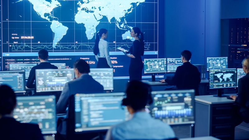 Diverse Team in a High-tech Control Room Analyzes Global Data on Multiple Screens, Ensuring Cybersecurity and Efficient Operations.