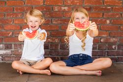 Cute Young Boy and Girl Eating Watermelon Against Brick Wall