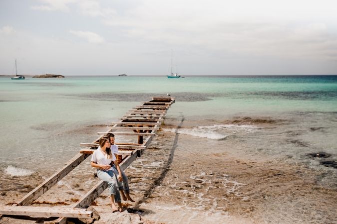 Glad lovers sitting on destroyed pier on seashore