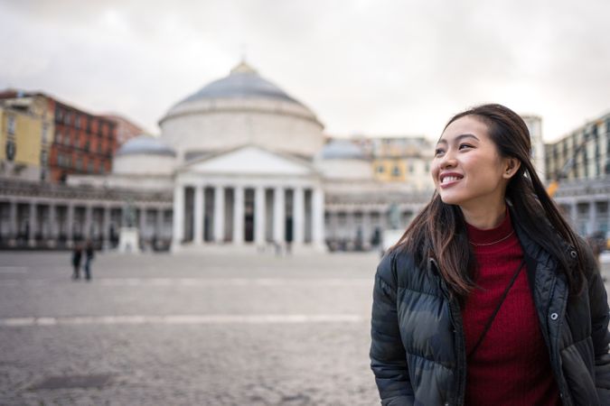 Joyful Asian woman on vacation in warm wear walking at old square with beautiful temple