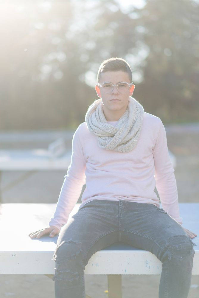 Smiling teenage male in striking eyewear sitting on bench in a city park