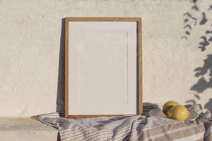 Blank vertical wooden frame picture mock up in sunlight with cotton throw, blanket and fresh lemons