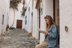 Side view of young woman sitting on window ledge with a paper map