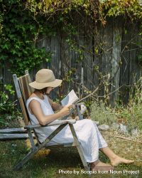 Woman with hat sitting on wooden chair and reading book at the garden 5ryMM0