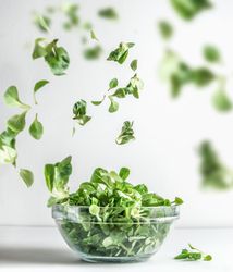 Green salad in glass bowl and flying lettuce leaves