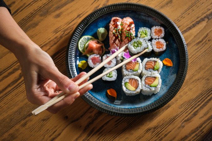 Person taking sushi with chopsticks from plate