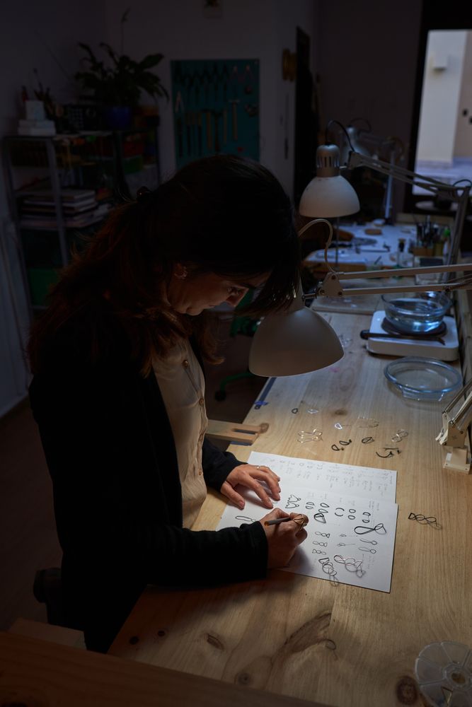Female master painting jewelry sketches in dark workshop