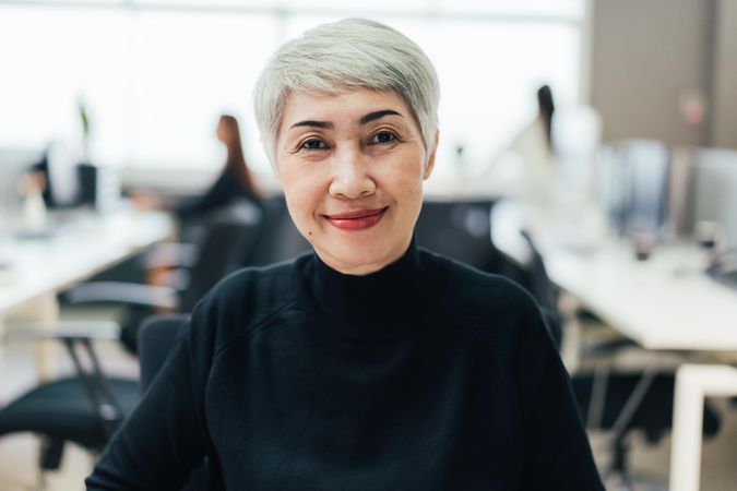 Grey haired woman smiling into camera in office