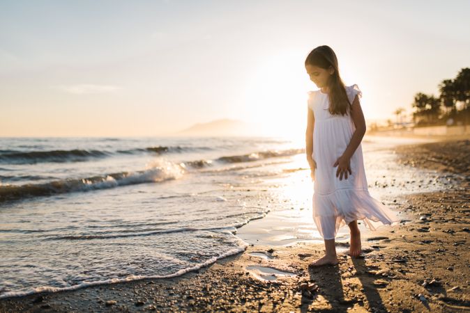 Adorable girl walking and playing on seaside at sunset